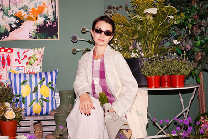 Woman wearing a pink checked dress with a light jacket in a floral interior setting