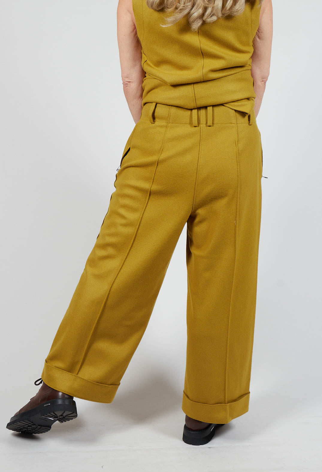 behind shot of lady wearing mustard carmi trousers with brown chunky boots and matching vest